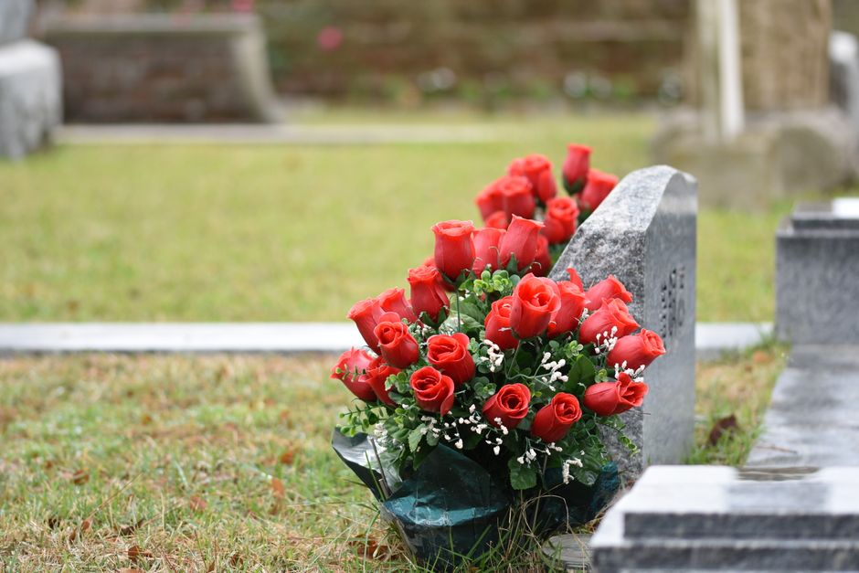 A floral gift of fresh, vibrant red roses with tightly closed buds and delicate petals, arranged in a cascading bouquet with lush green foliage and small white baby's breath accents. The bouquet is wr