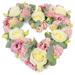 A lush, heart-shaped wreath of pastel flowers is displayed against a bright white background, its soft colours and rounded form radiating calm and compassion. At the core of the design are large, creamy roses in shades of ivory and pale yellow, each rose carefully opened so the layered petals form elegant, rounded cups that anchor the eye. Filling the spaces between them are clouds of soft pink carnations, their ruffled petals packed closely together, creating a rich, tactile surface that feels both gentle and embracing. Nestled among these are deeper pink and mauve lisianthus, their more open, gently flared blooms lending a flowing rhythm and a subtle depth of tone, like quiet shadows at dusk. Interwoven eucalyptus stems bring structure and serenity, their silvery-green, coin-shaped leaves lying cool against the petals and suggesting the peaceful greenery that surrounds many corners of Noak Hill. Small yellow-green buds punctuate the arrangement, adding youthfulness and a sense of ongoing life to the tribute. The heart itself is symmetrical and clearly defined, with no gaps, giving the impression of completeness and unwavering love. Emotionally, the wreath feels thoughtful and consoling, a design well suited to funeral services, memorials, or anniversary remembrances held by families in Noak Hill. It could easily be imagined resting beside a casket or placed near a memorial book, its pastel palette of creams, pinks, and greens offering a gentle, visual language of sympathy, remembrance, and enduring affection during times of loss.